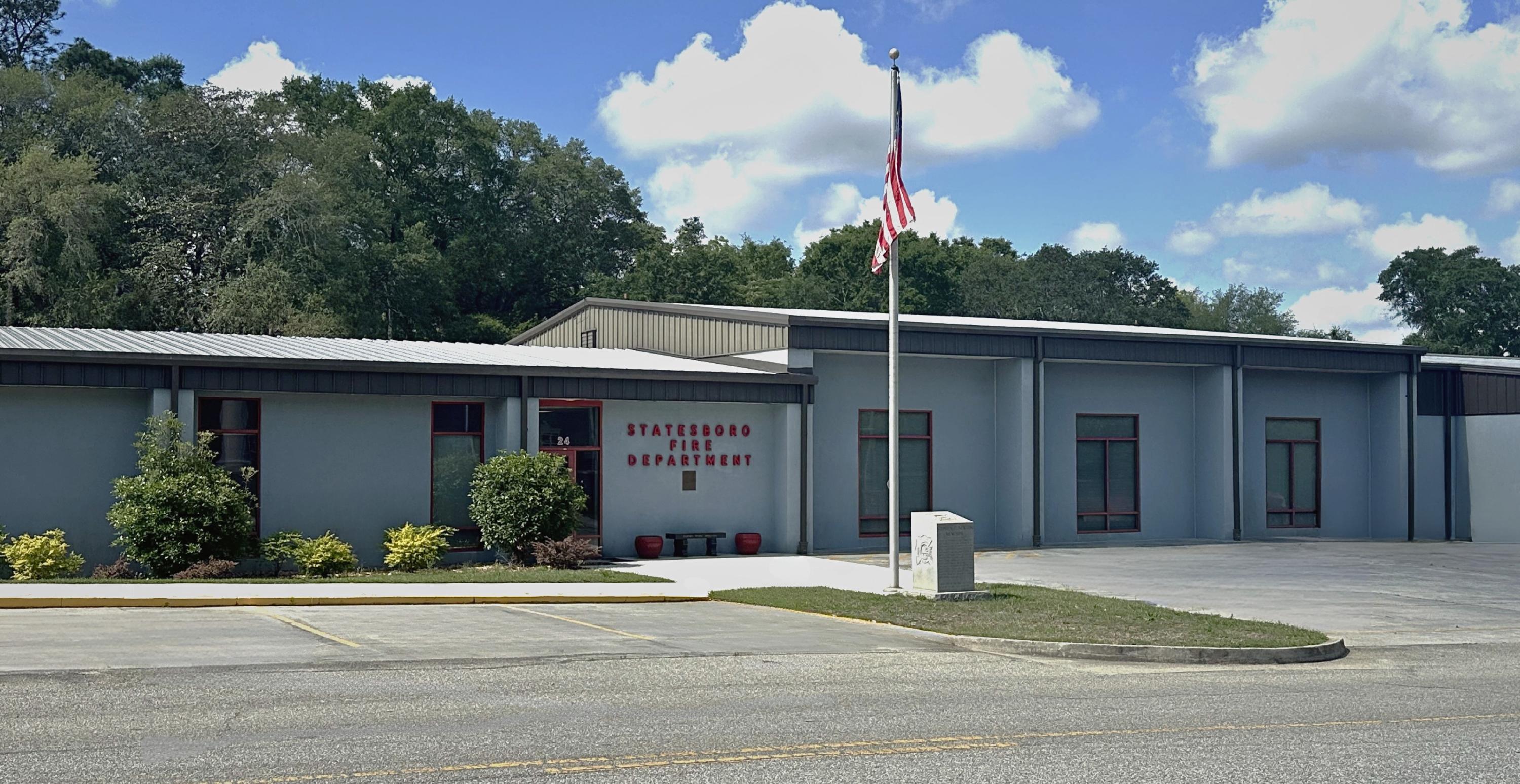 Gray Blue Building with Red Trim with a parking lot and American flag pole out front